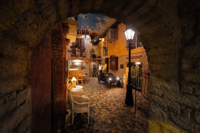 Step into the enchanting lobby of Paul's Fantasia Boutique Suites, where Italian flair meets vintage charm. With cobblestone paths lit by antique lamps, a star-sprinkled ceiling, and a classic car centerpiece, this magical entrance ushers you into an unforgettable luxury stay in the heart of Stettin. Discover a hotel experience that's truly like no other.